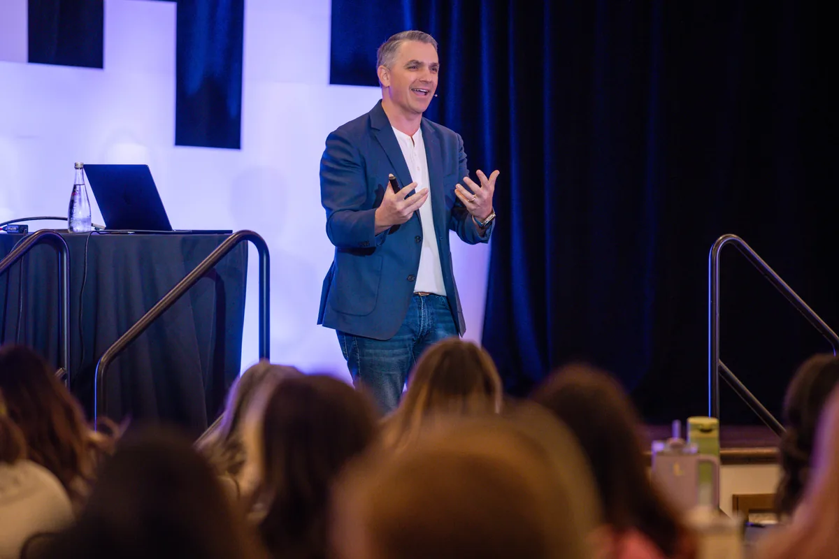 Ryan Deiss speaking on stage, audience in the foreground